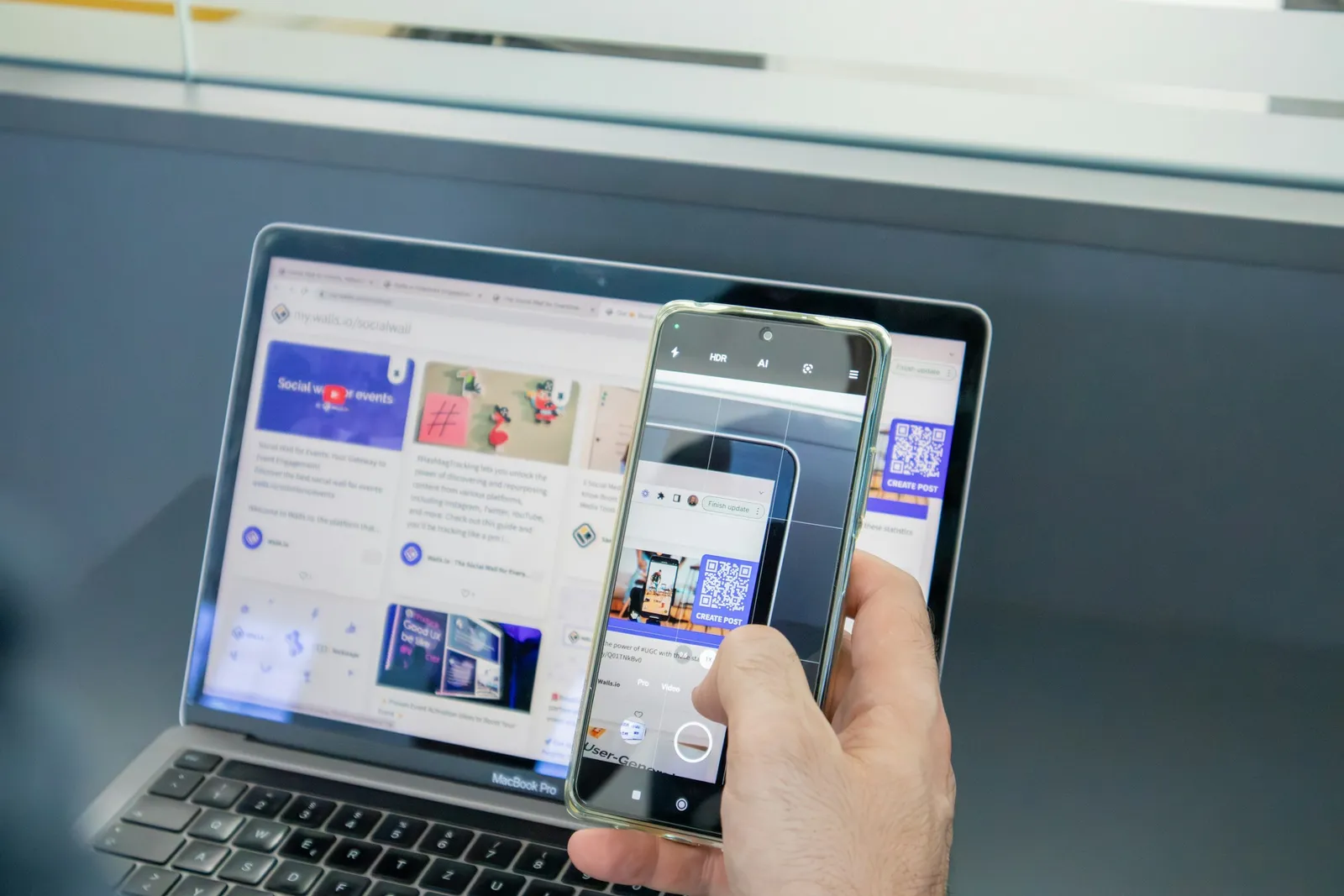 Une main tient un smartphone qui scanne un QR code affiché sur l'écran d'un ordinateur portable.