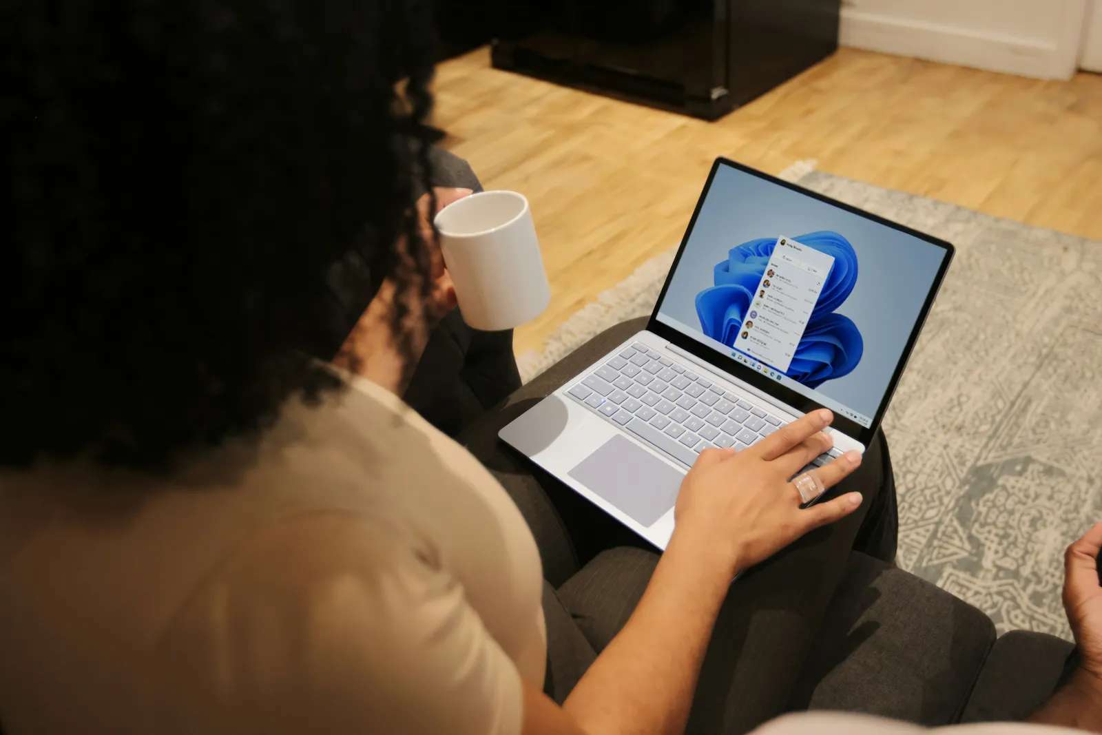 Une personne assise dans un canapé, une tasse à la main, travaille sur un ordinateur portable sous Windows.