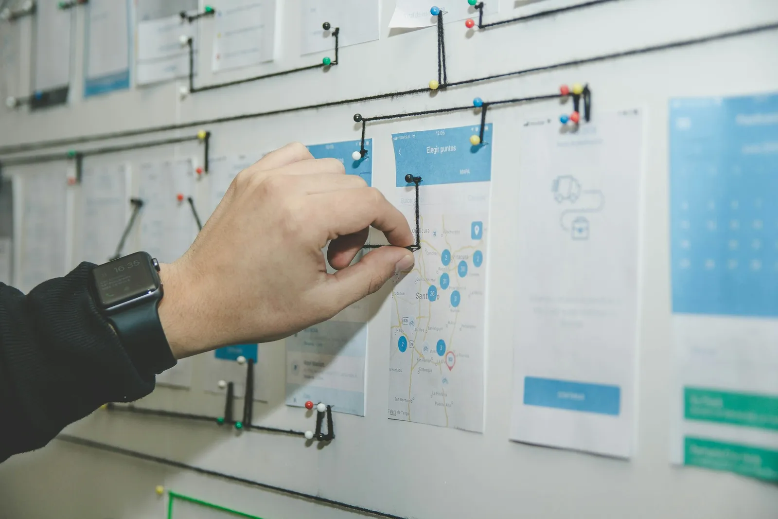 A hand places a string between pinned sheets on a planning wall.